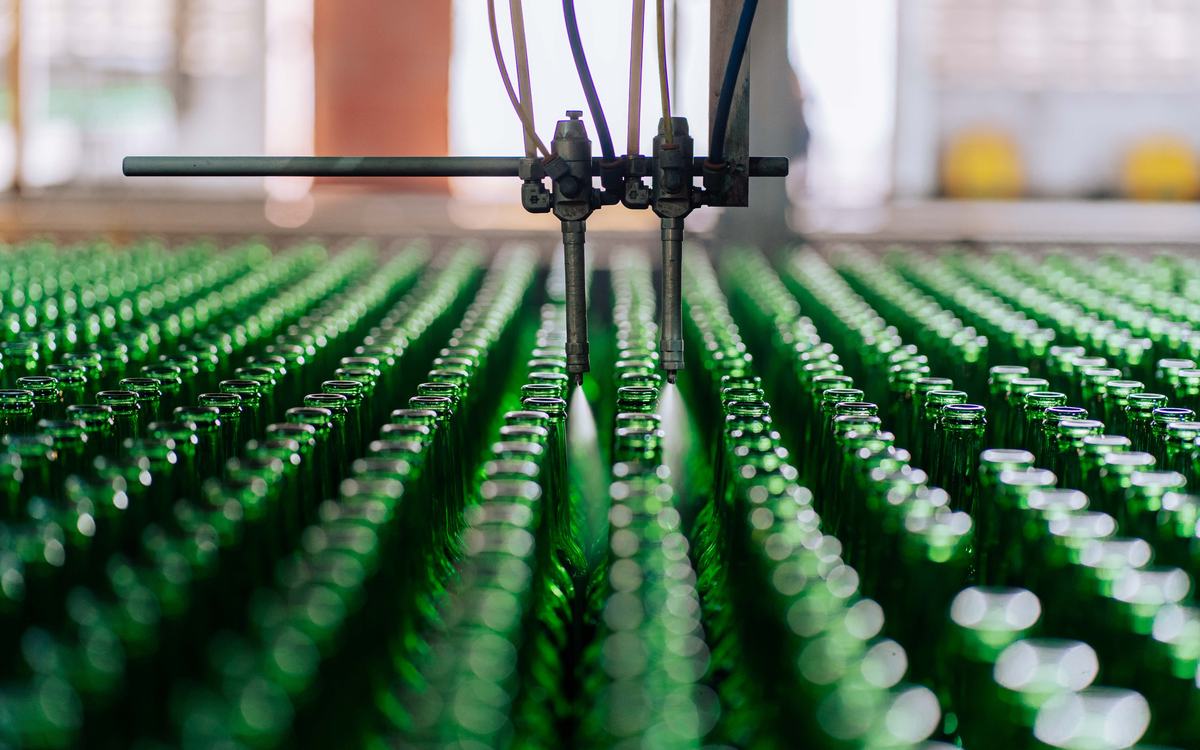 Automated line spraying rows of green glass bottles